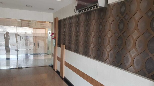 A hotel corridor with a patterned wall, a wooden bench, and a glass door leading to another room. - Hotel Janardana (Udupi)