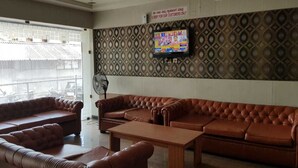 A lobby with a brown leather sofa, a wooden coffee table, and a TV mounted on the wall. - Hotel Janardana (Udupi)