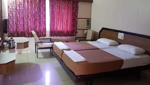 A hotel room with two beds, a desk, and a chair. - Hotel Janardana (Udupi)