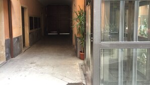 Un pasillo estrecho con una puerta cerrada al final, una planta en maceta y una puerta de cristal a la derecha.