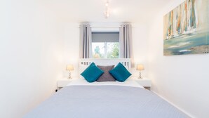 Une chambre bien rangée, avec un grand lit, deux tables de chevet avec des lampes, une fenêtre avec des rideaux et un tableau accroché au mur.