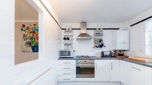 Une cuisine moderne avec des armoires blanches, une cuisinière à gaz, un four et un four à micro-ondes. Une fenêtre offre une vue sur l’extérieur.