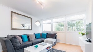 Un salon moderne avec un canapé d’angle gris, une table basse blanche et une grande fenêtre laissant entrer la lumière naturelle.