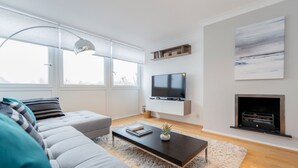 Un salon moderne avec un canapé, une table basse, un téléviseur et une cheminée.