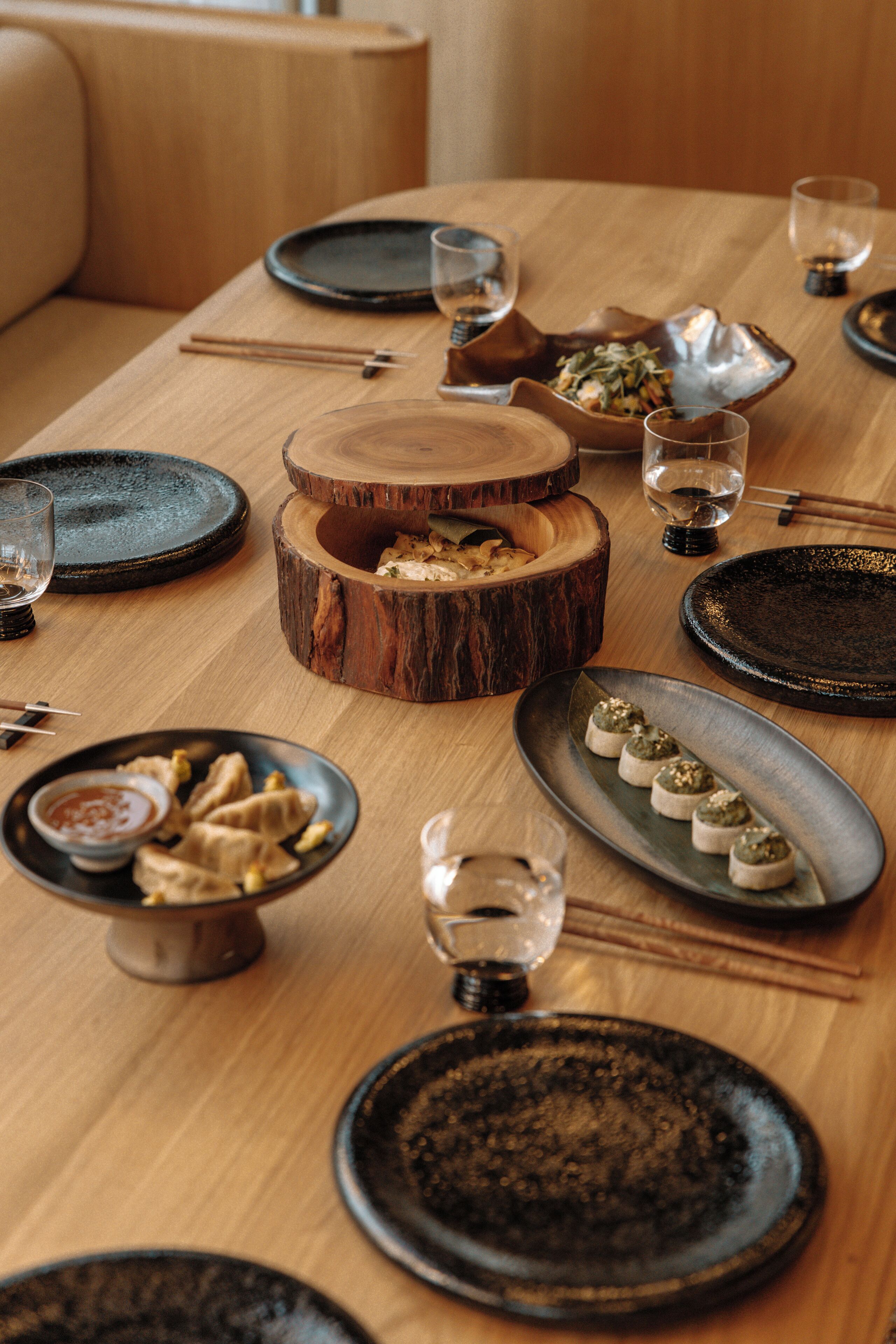 A dining table set with various dishes, including a bowl of dumplings, a plate of appetizers, and a wooden bowl with food.