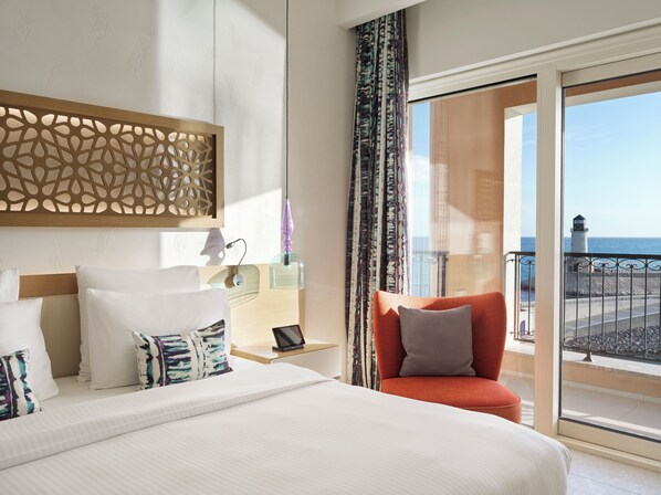 Habitación de hotel con cama, una silla, mesita de noche y vista al mar.