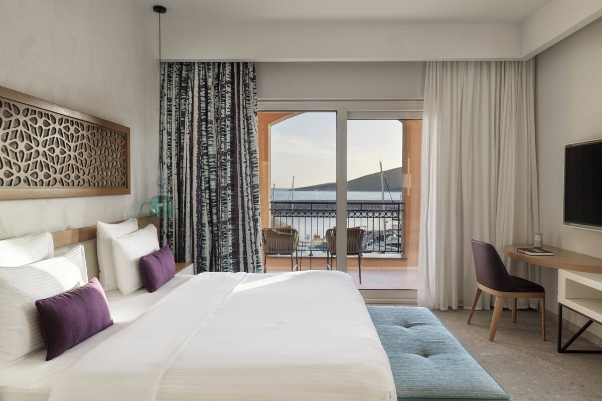 A hotel room with a large bed, a desk, a chair, and a view of the sea.
