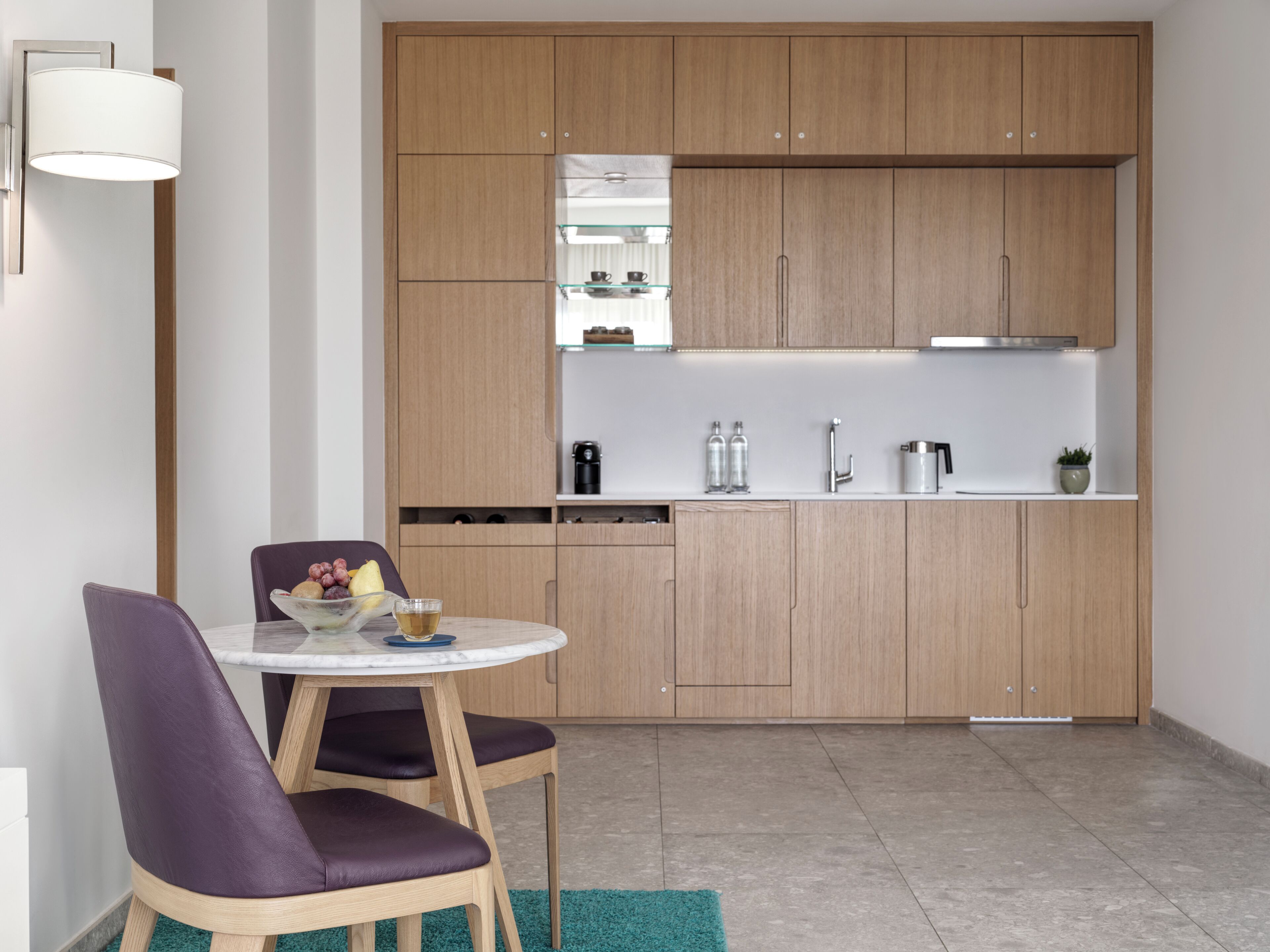 Una cocina moderna con armarios de madera, una encimera blanca y una mesa de comedor redonda con sillas moradas.