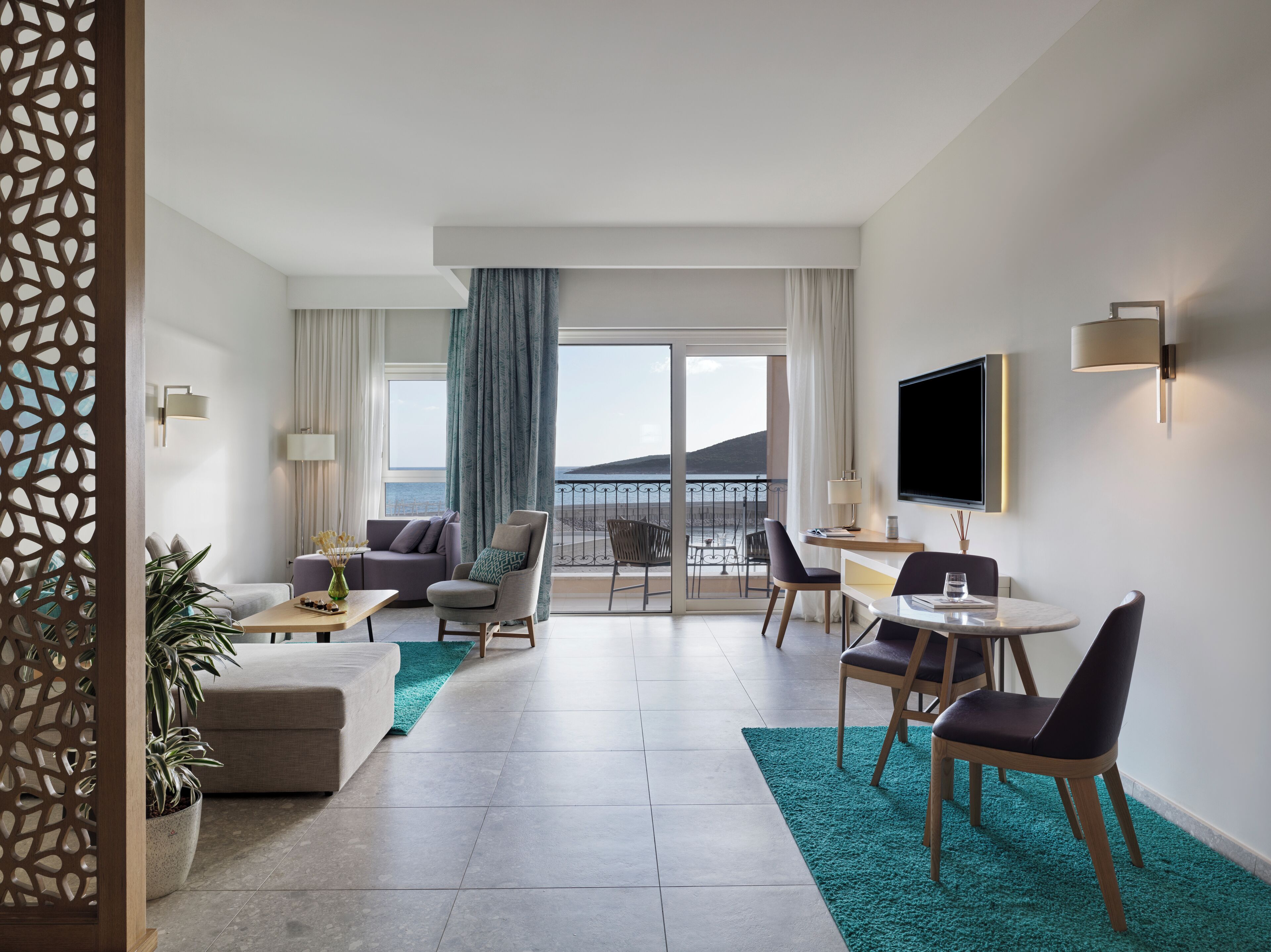 Een moderne hotelkamer met balkon, een bank, een eethoek en een televisie.