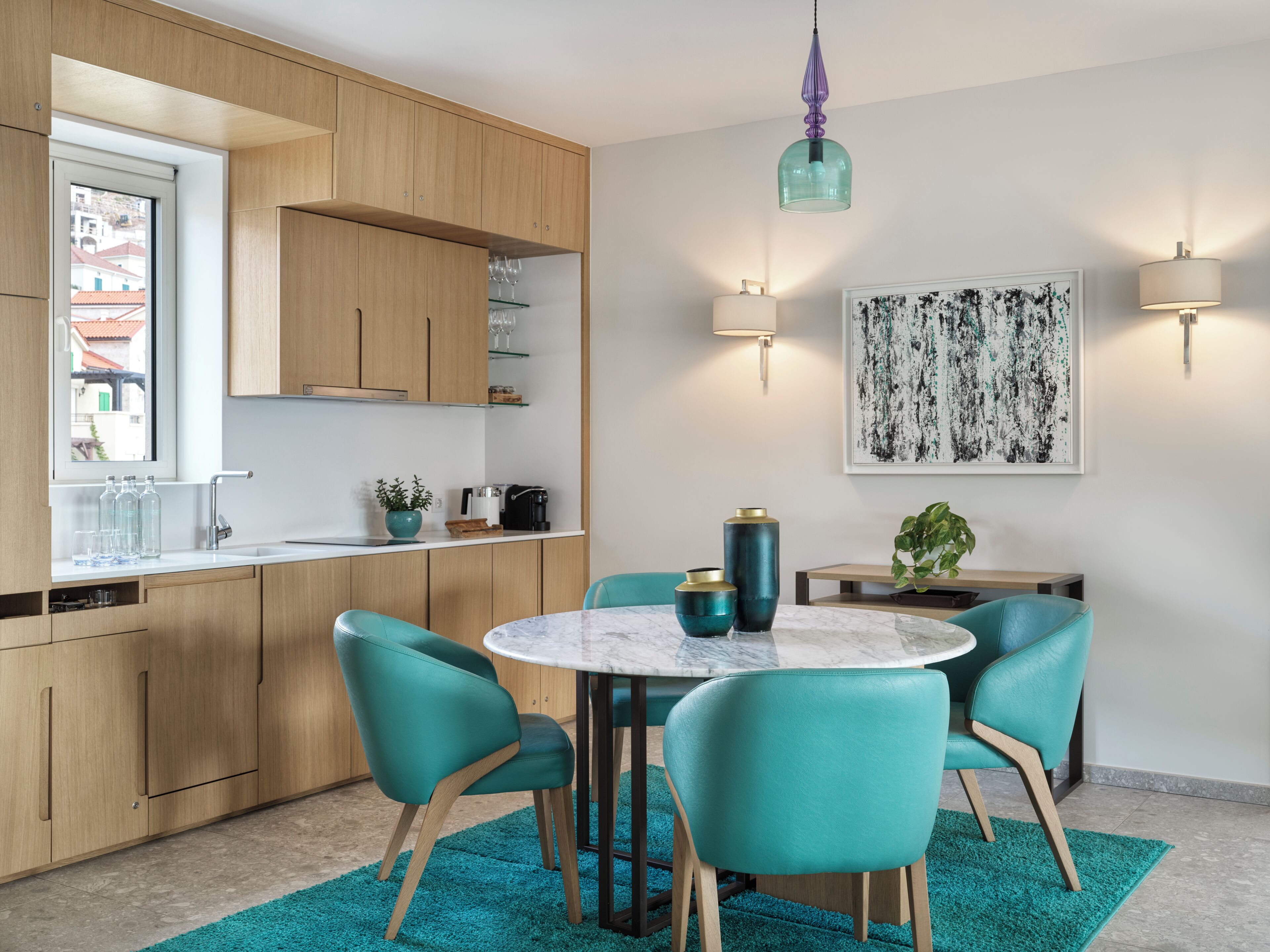 A modern kitchen with wooden cabinets, a marble island, teal chairs, and pendant lighting.