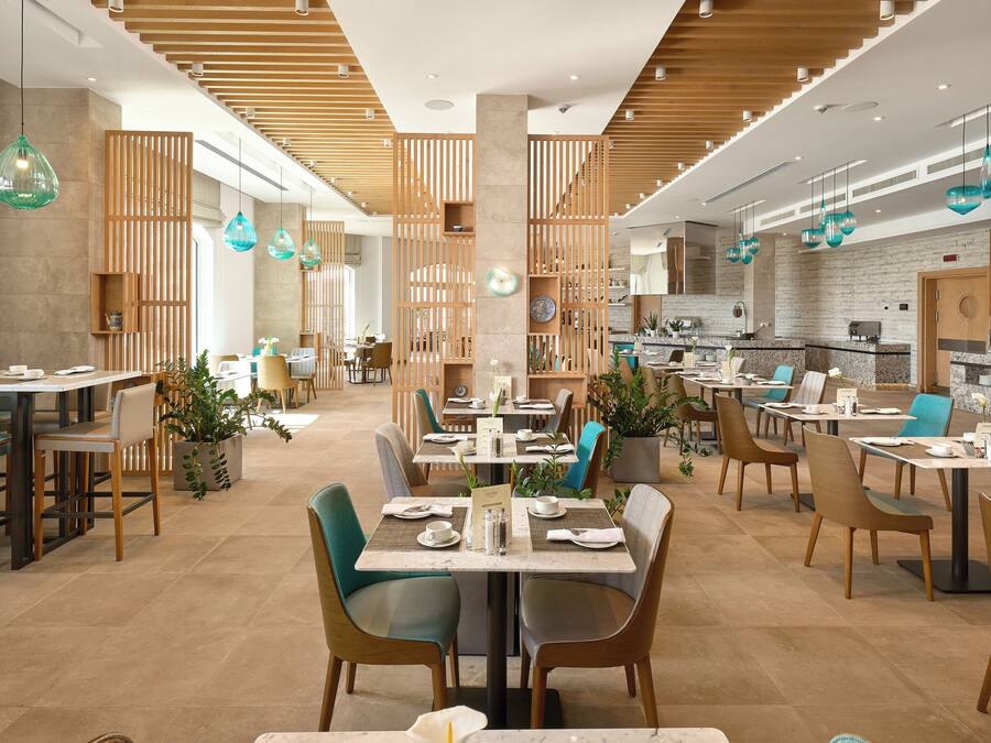 A modern restaurant with wooden accents, green chairs, and pendant lighting.