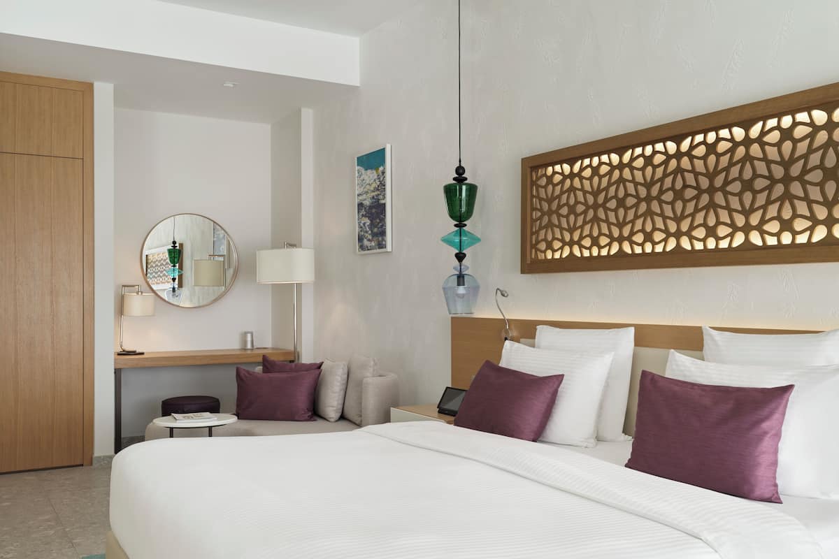 A hotel room with a large bed, a desk with a lamp, a mirror, and a decorative headboard.