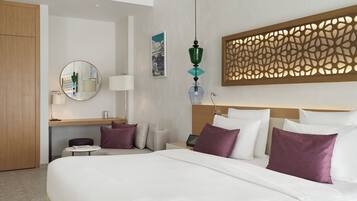 Habitación de hotel con una cama grande, un escritorio con lámpara, un espejo y un cabecero decorativo.