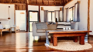 Amplia sala de estar con techo de madera, un conjunto de sofás, una mesa de centro y un ventanal con cortinas.