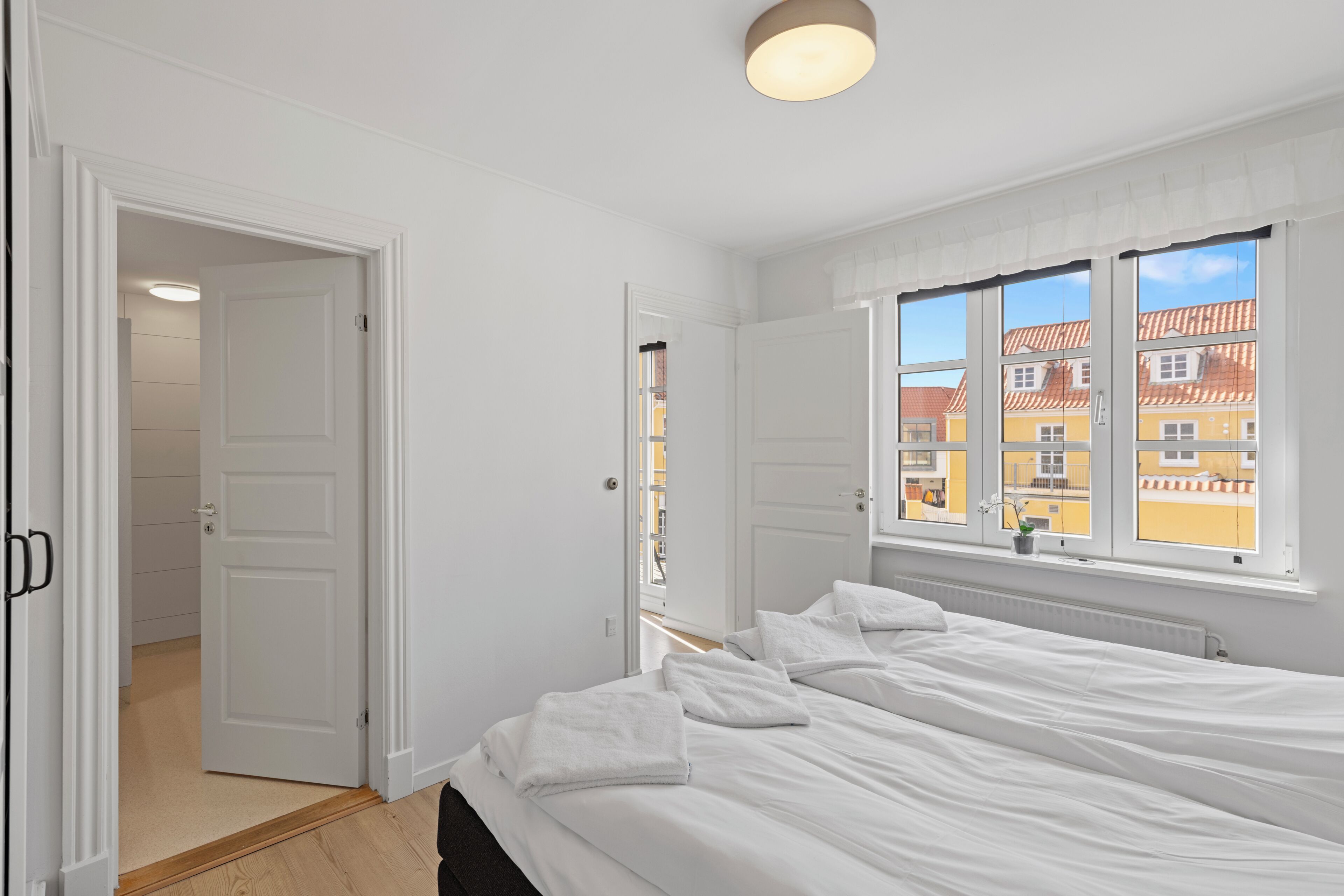 A bedroom with a bed, a window with a view, and a door leading to another room.