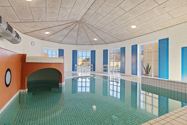 Una piscina con suelo de baldosas, techo con lámpara central y contraventanas azules en las ventanas.