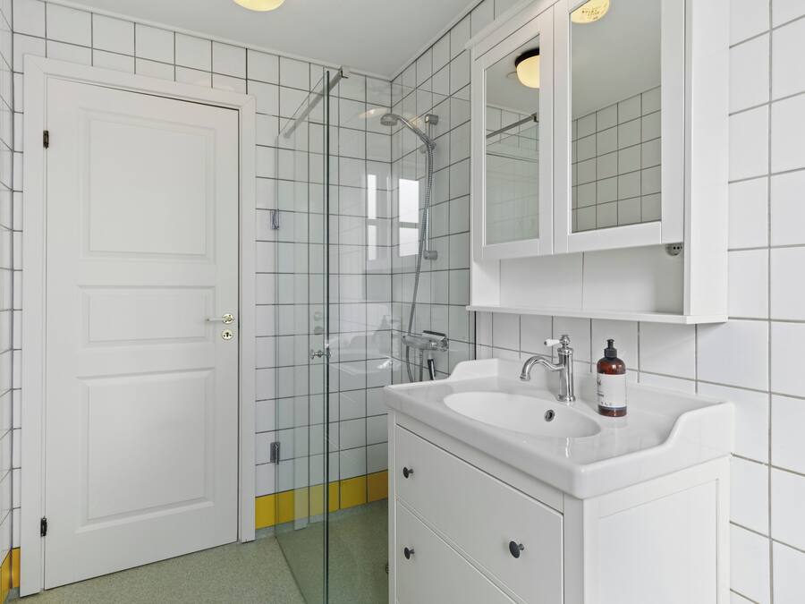 Une salle de bain avec un lavabo blanc, un miroir et une cabine de douche en verre.