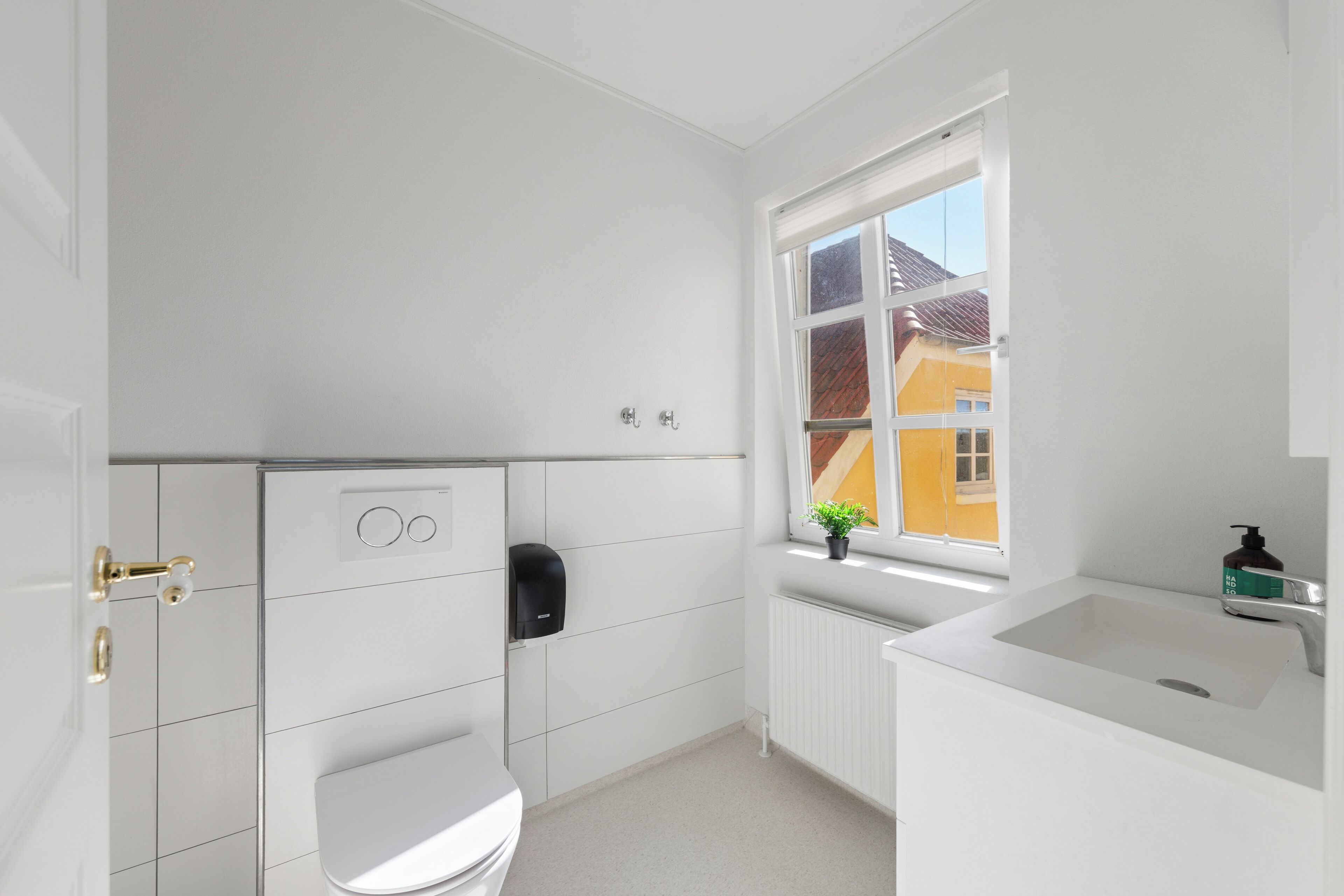 A modern bathroom with a toilet, a hand dryer, and a window with a view of a yellow building.