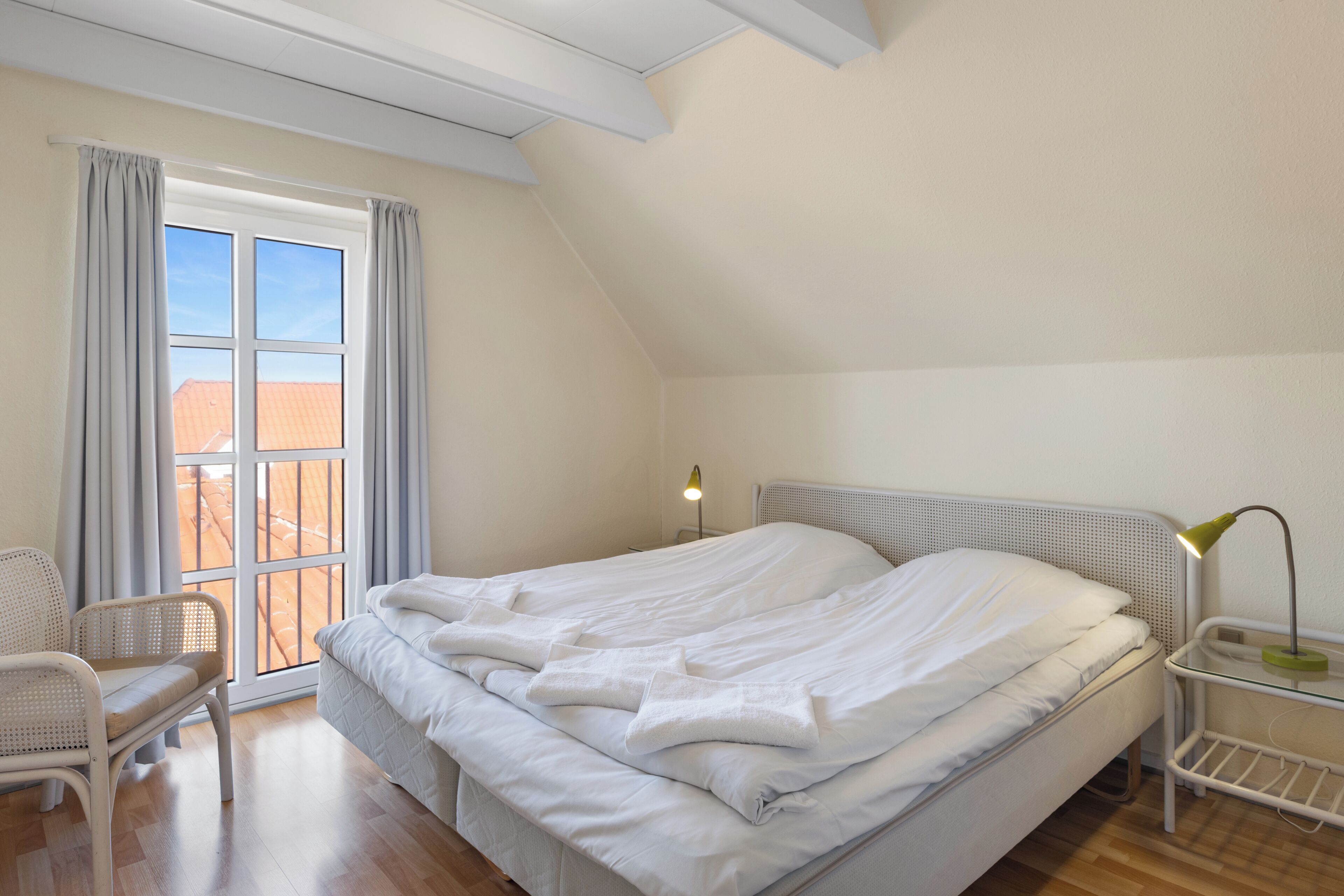 Une chambre à coucher avec un lit, une chaise, une table de chevet avec une lampe et une fenêtre avec des rideaux.
