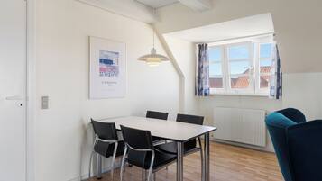 A room with a dining table, chairs, a pendant light, a window with curtains, and a radiator.