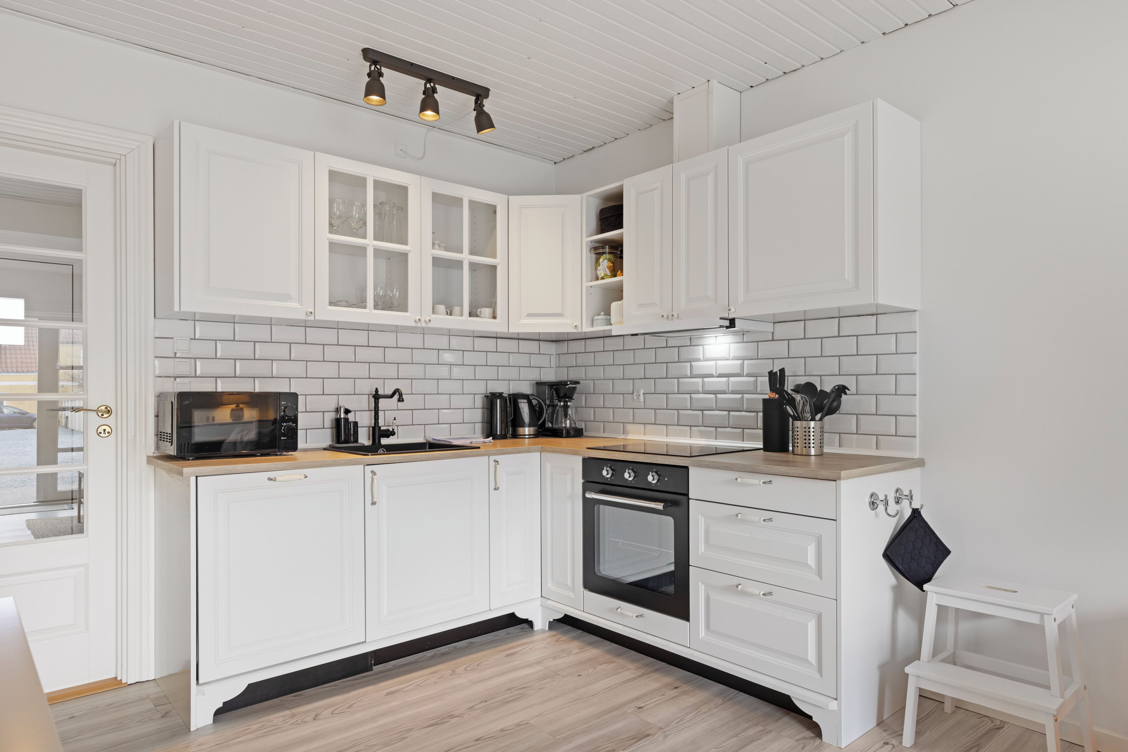 A modern kitchen with white cabinetry, a microwave, an oven, and a coffee maker.