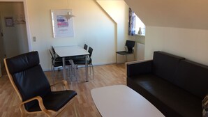 Een moderne woonkamer met een zwarte leren bank, een houten stoel, een witte tafel en een eethoek met een witte tafel en stoelen.