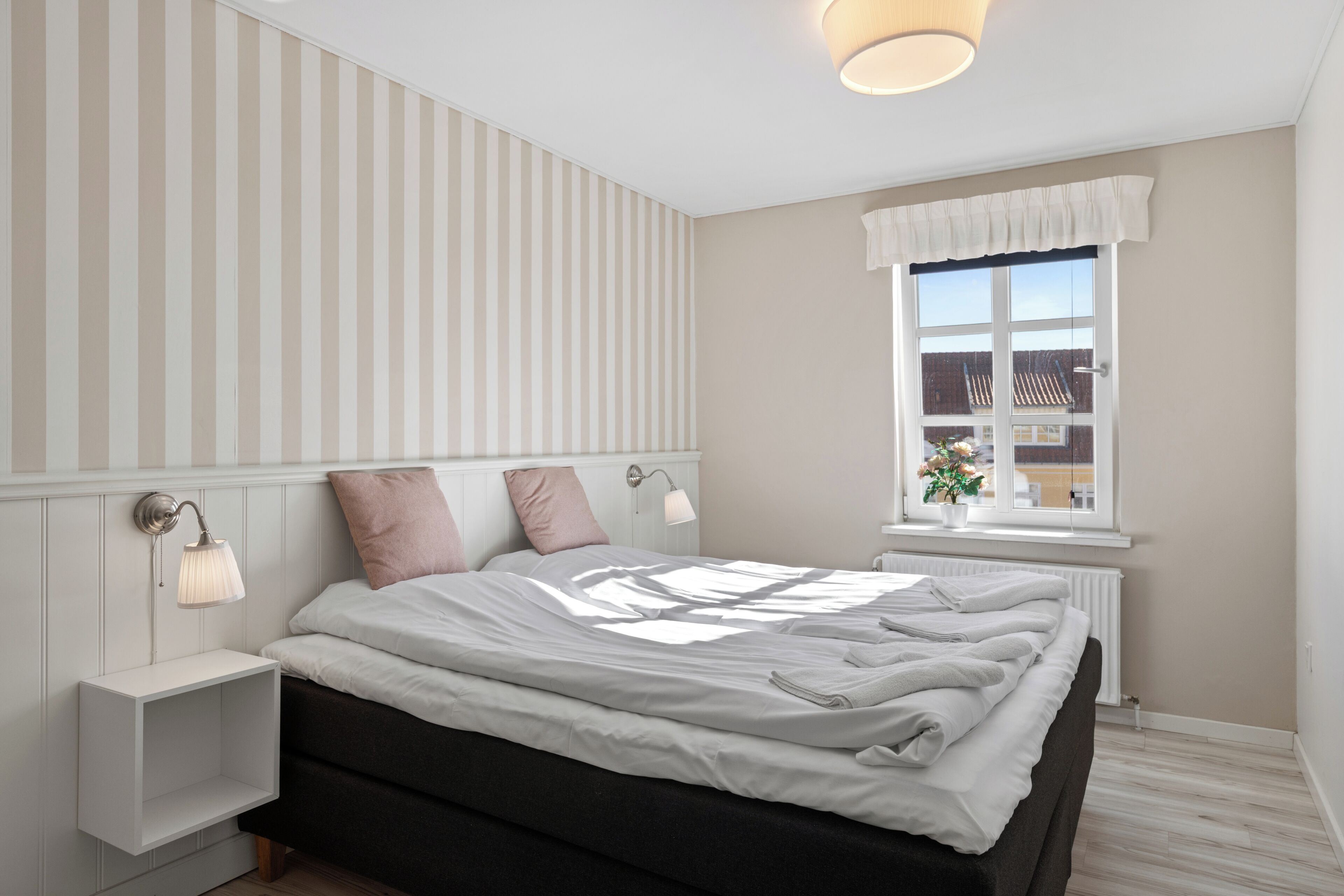A bedroom with a bed, bedside lamps, a window with a view, and a radiator.