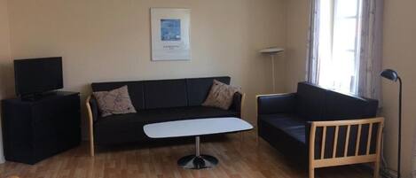 Un salon comprenant un canapé, une table basse, un téléviseur posé sur un meuble et une lampe sur pied.