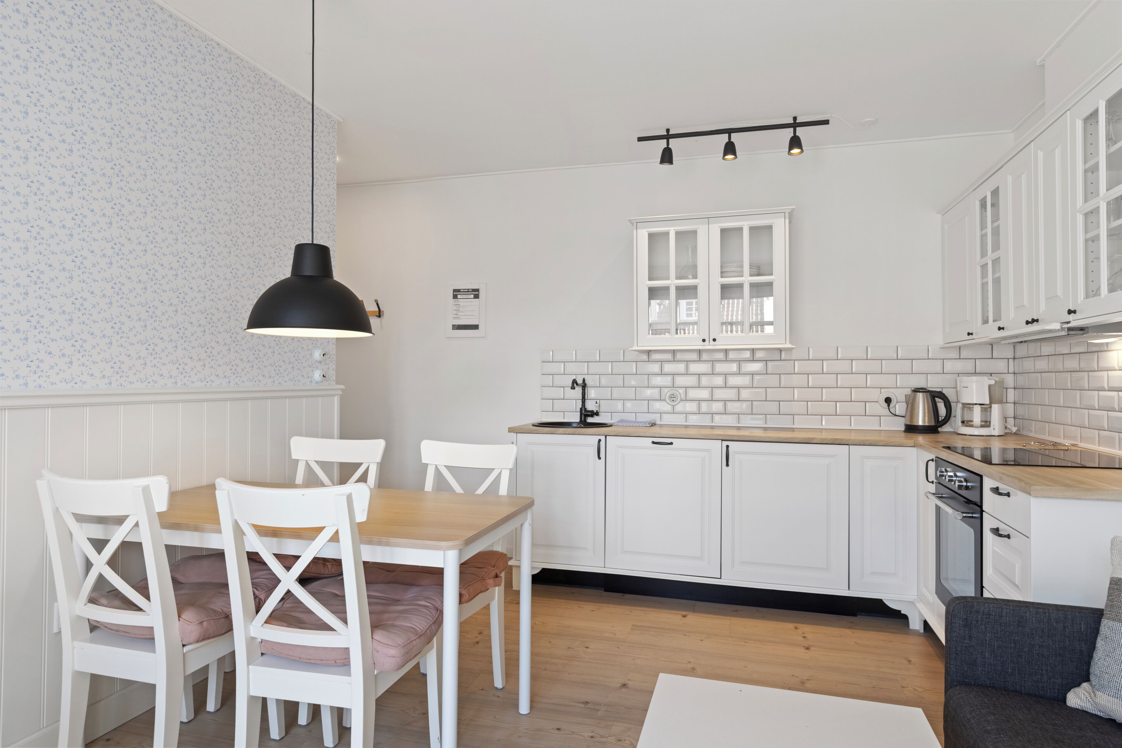 Una cocina moderna con gabinetes blancos, encimera de madera y una zona de comedor con sillas blancas.