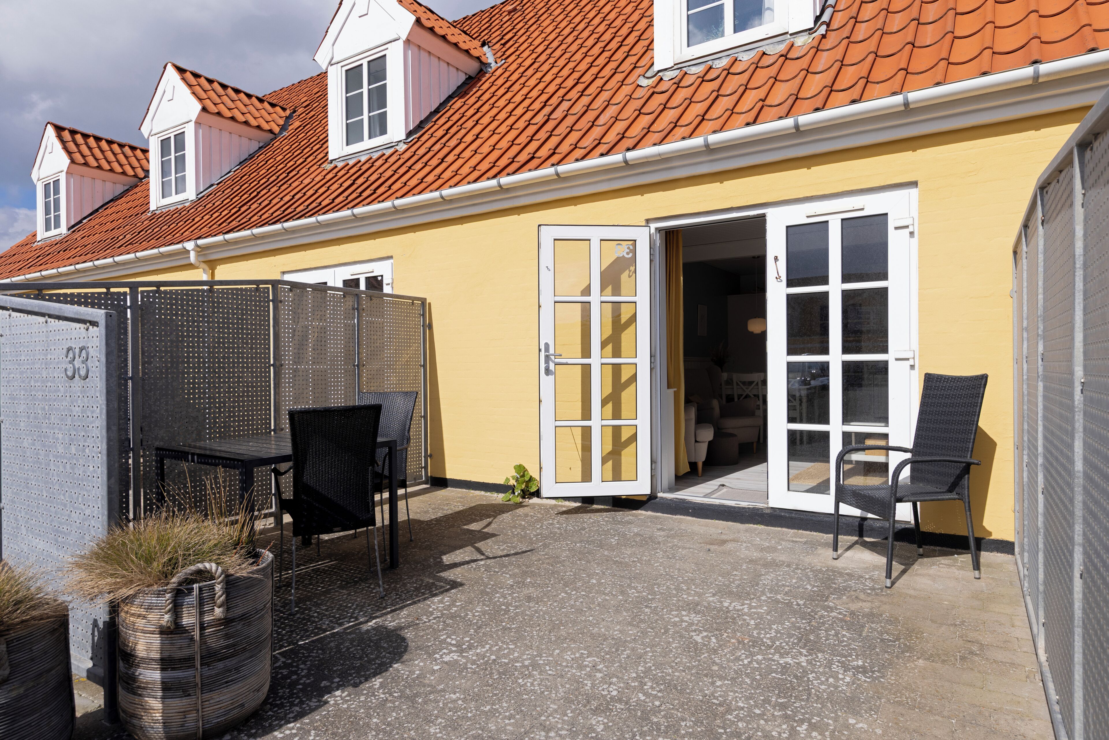 Een geel gebouw met een pannendak, een overdekte patio met stoelen en een schuifdeur van glas.