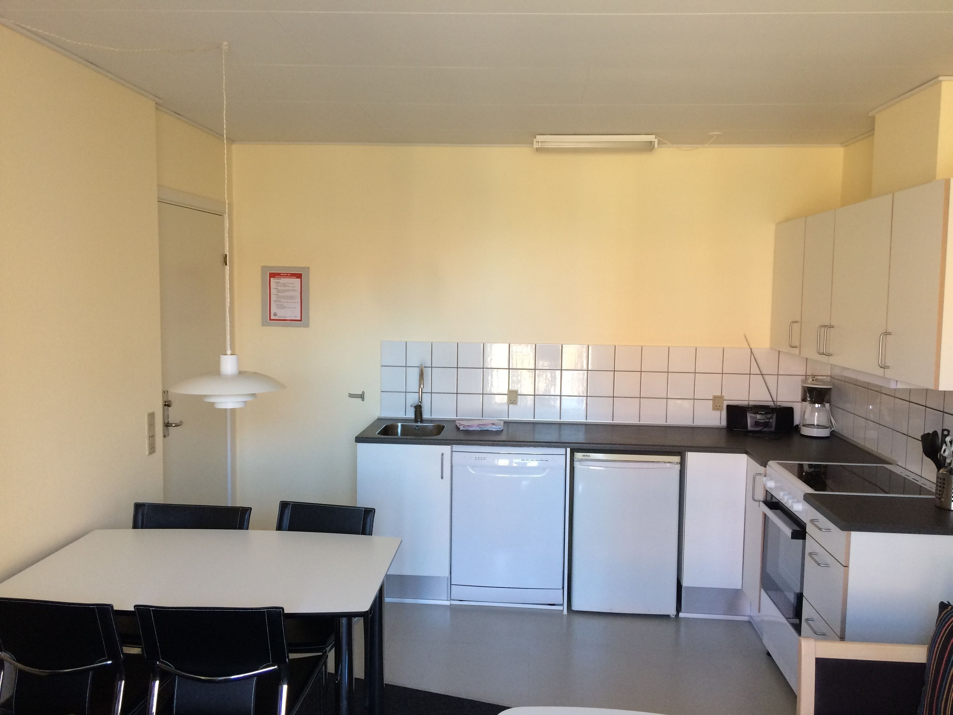 A compact kitchen with white cabinets, a sink, a dishwasher, and a dining area with a table and chairs.