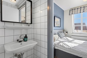 Een badkamer met een witte wastafel, spiegel en een raam met uitzicht op gebouwen.