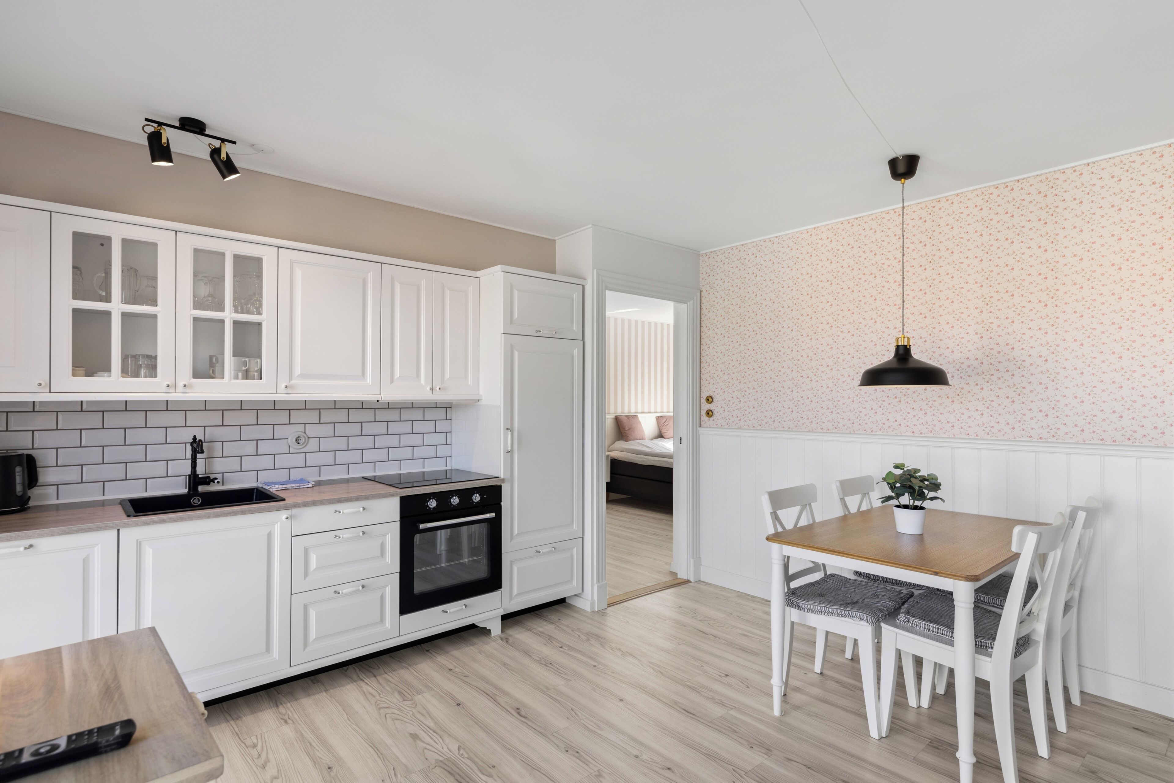 A modern kitchen with white cabinets, a black oven, and a wooden dining table with chairs.