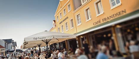 A busy outdoor café with tables and umbrellas, surrounded by historic buildings.