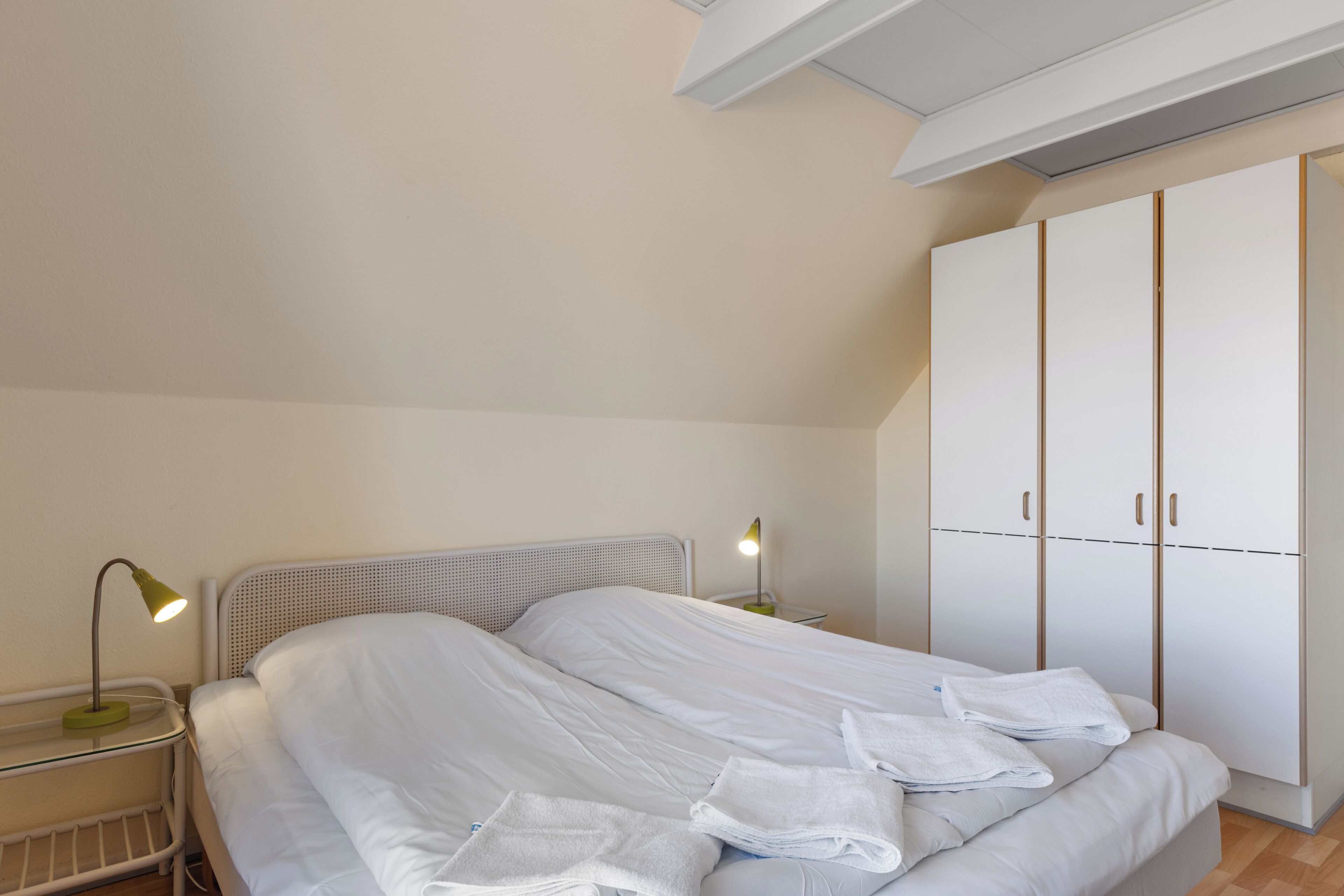 A bedroom with a bed, two bedside tables with lamps, a wardrobe, and a ceiling light.