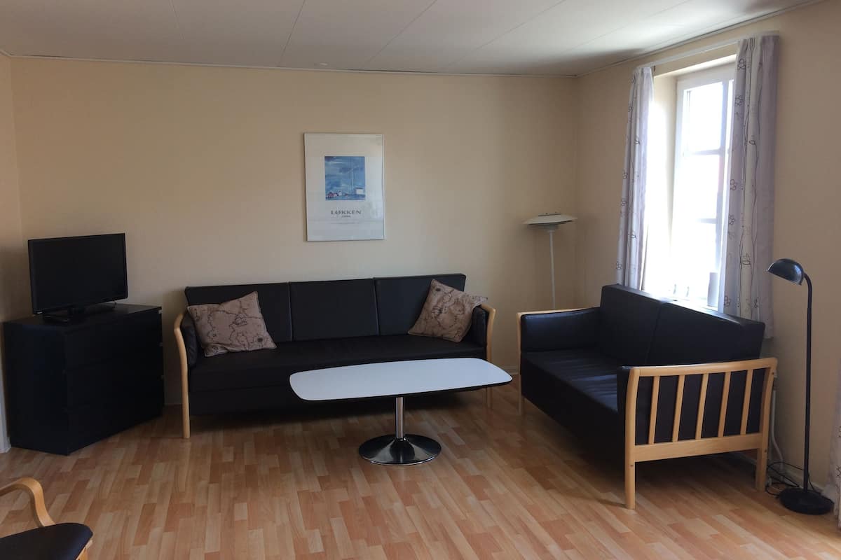 Un salon moderne avec un canapé, une petite table, un téléviseur et une lampe.