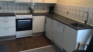Een kleine keuken met witte kastjes, een fornuis, een vaatwasser en een spoelbak.