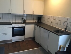 A compact kitchen with white cabinets, a stove, a dishwasher, and a sink. - Løkken Badehotel - Apartment Hotel (Lokken)