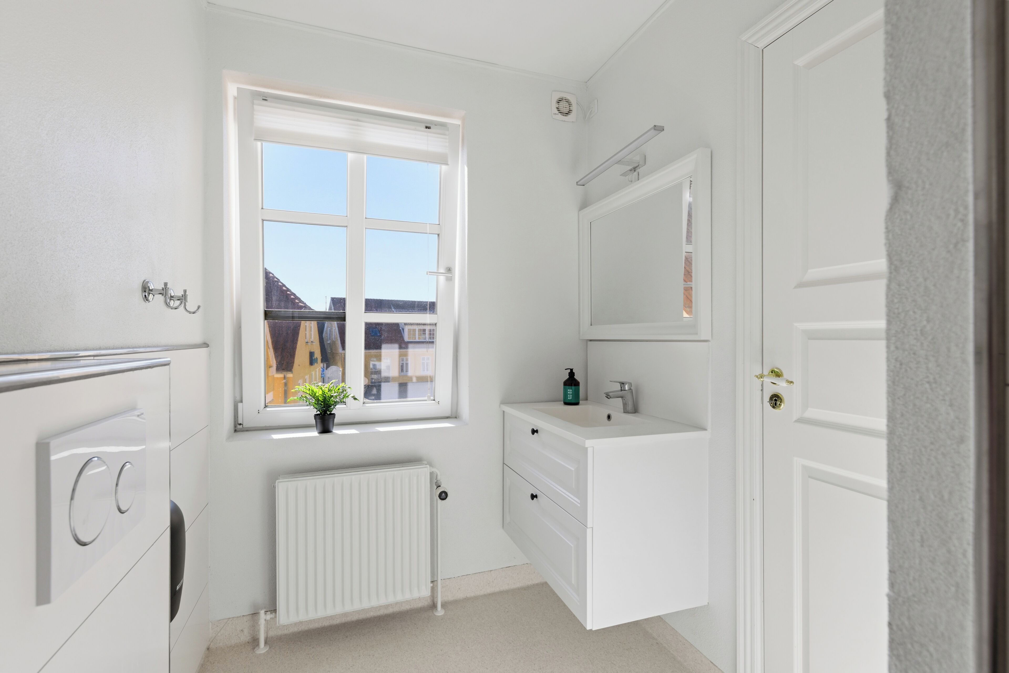 Un baño blanco con ventana, radiador, lavabo y espejo.