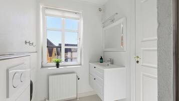 Un baño blanco con ventana, radiador, lavabo y espejo.
