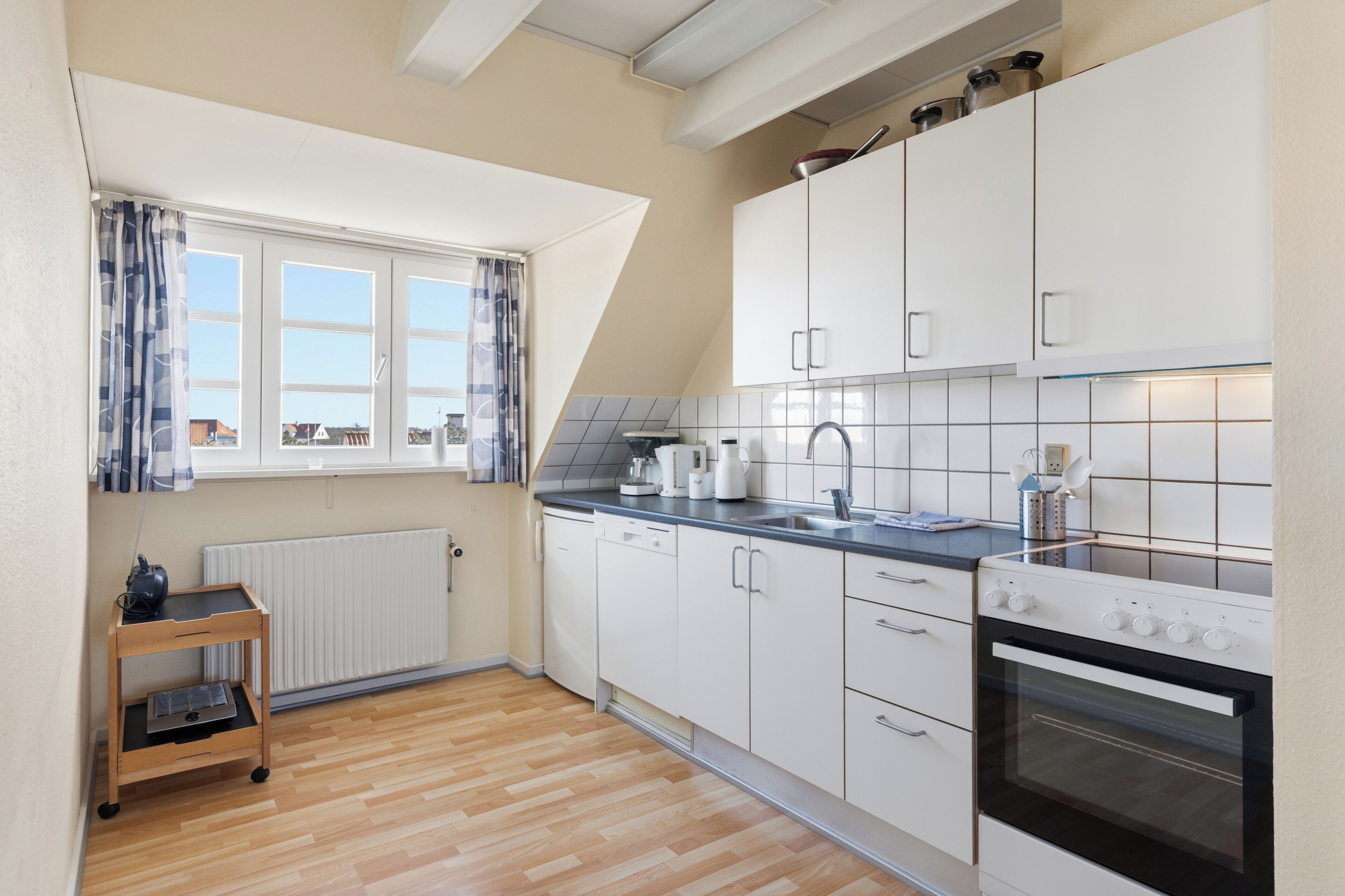 Una cocina moderna con armarios blancos, horno empotrado y una ventana con cortinas.