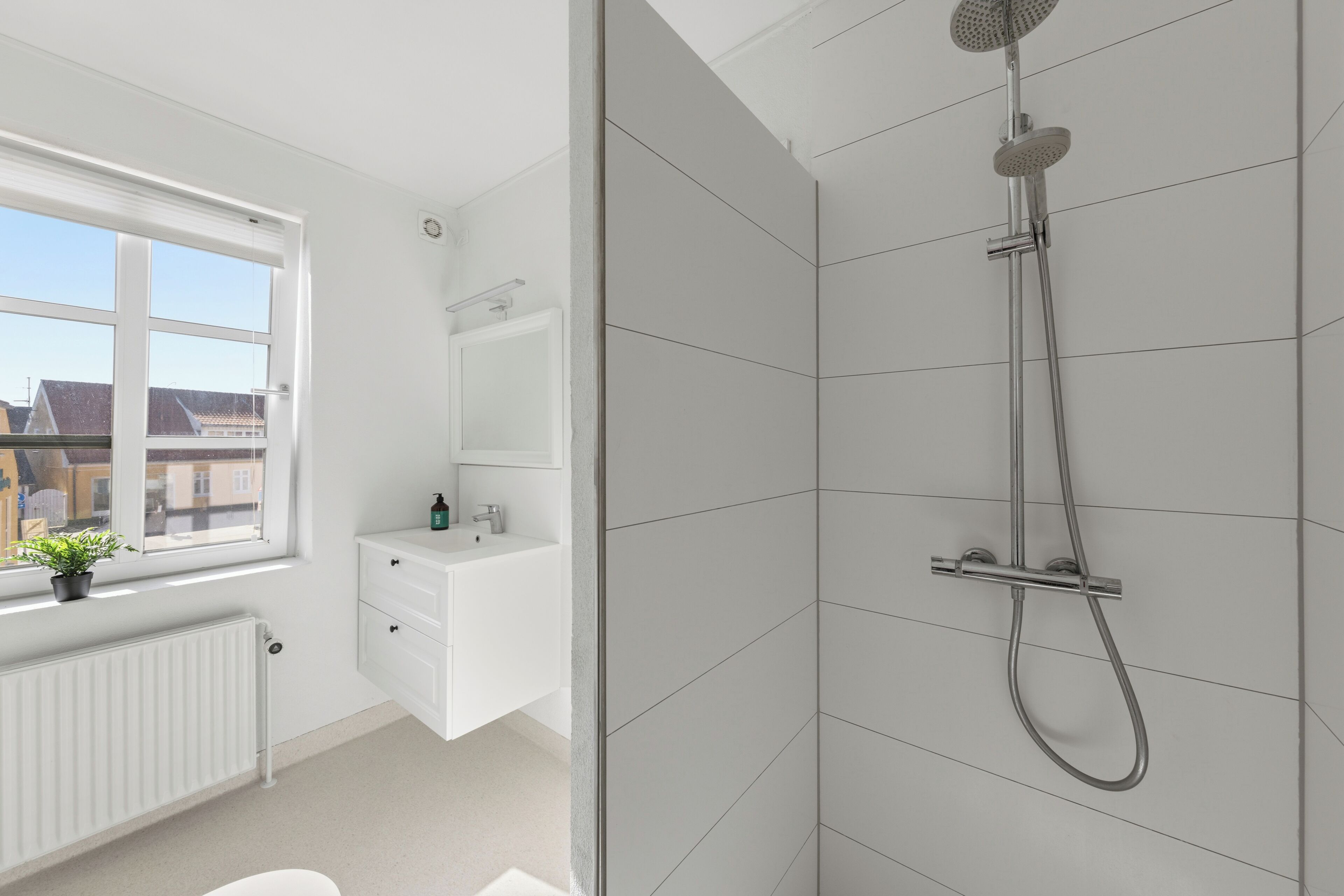 A modern bathroom with a shower, a window, a radiator, and a sink.