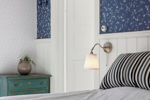 Een slaapkamer met een bed, een nachtkastje met een vaas, een wandlamp en een deur.