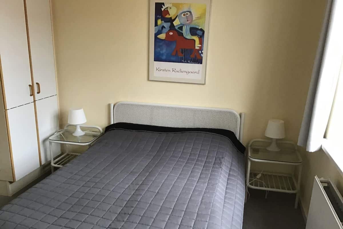 Une chambre à coucher avec un lit, deux tables de chevet avec des lampes, une armoire et un tableau encadré au mur.