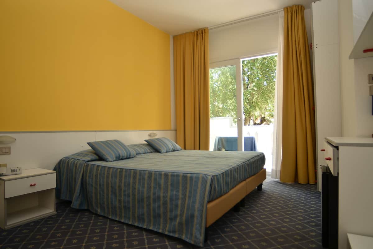A hotel room with a bed, a nightstand, a desk, and a window with curtains.