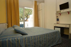 Ein Hotelzimmer mit Bett, Schreibtisch, Fernseher und einem Fenster mit Vorhängen.
