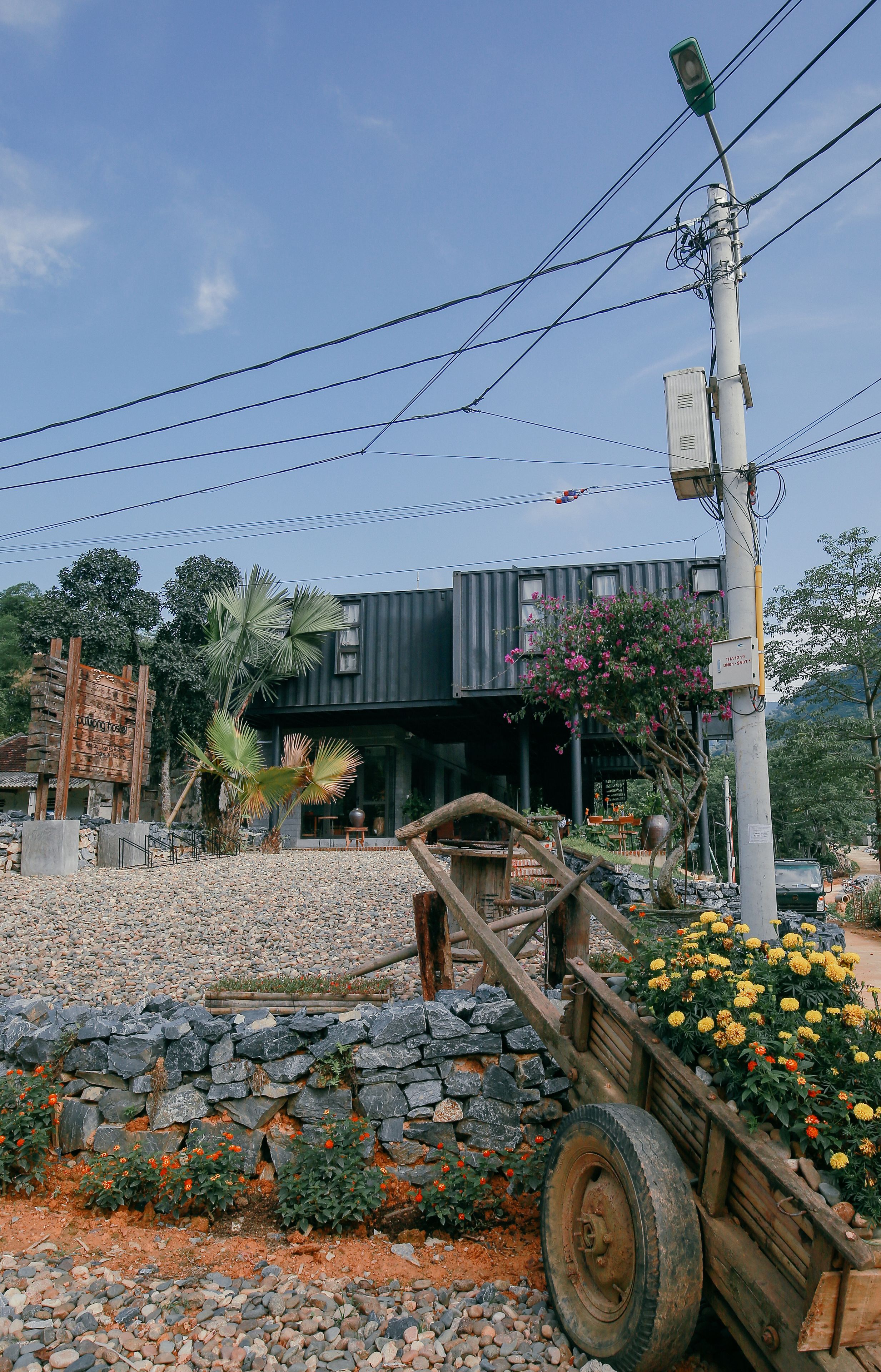A modern building with a stone wall and a wheelbarrow filled with flowers in front.