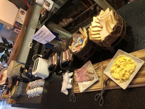 Un piano di lavoro della cucina con diversi alimenti, tra cui pane, uova e carne, oltre a utensili e elettrodomestici.