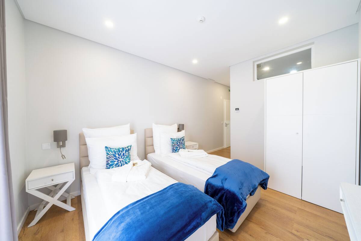 Een kamer met twee bedden, een witte garderobe, een klein nachtkastje met een lamp en een plafondlamp.