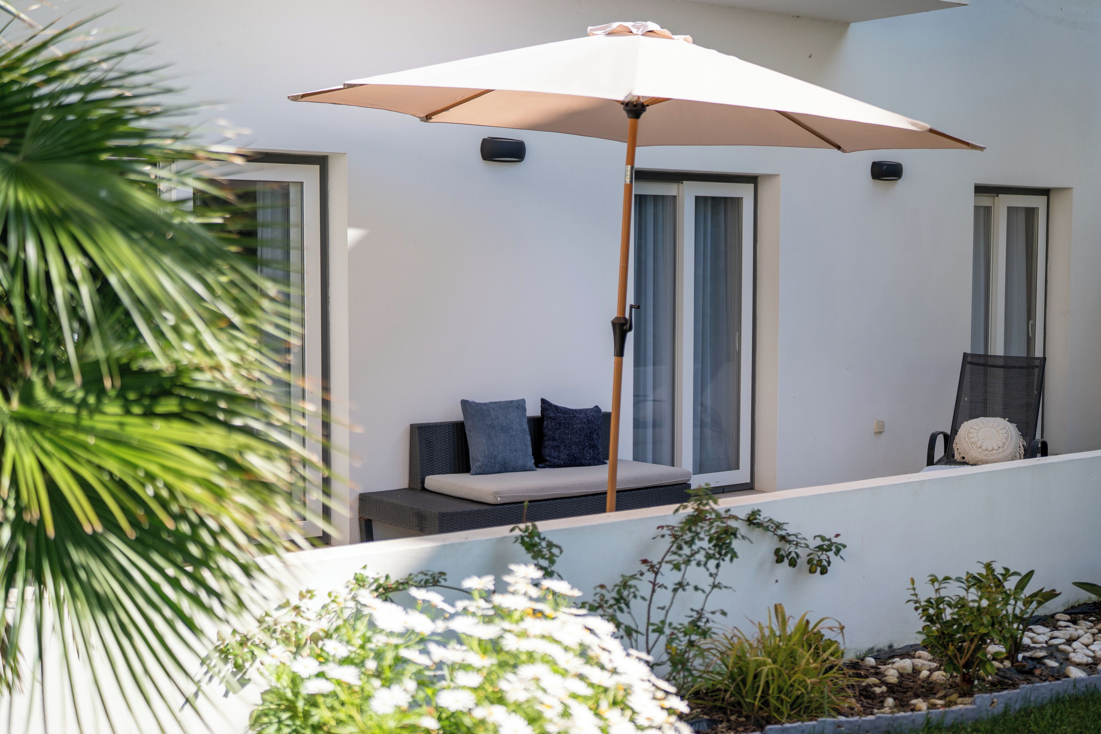 Un espace extérieur moderne, aménagé avec un banc rembourré, un grand parasol et offrant une vue sur un bâtiment doté de fenêtres.
